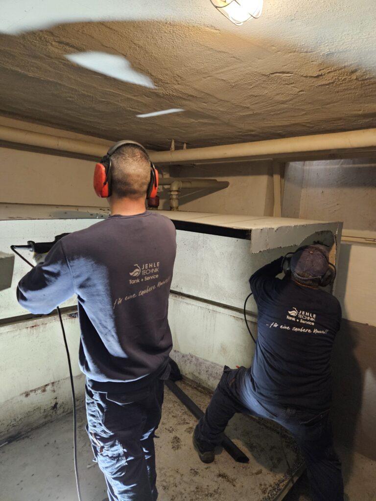 Zwei Männer mit blauen Shirts arbeiten konzentriert an einem großen Metallbehälter
